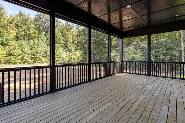 Covered deck with black metal railing and a dark wood ceiling facing the woods
