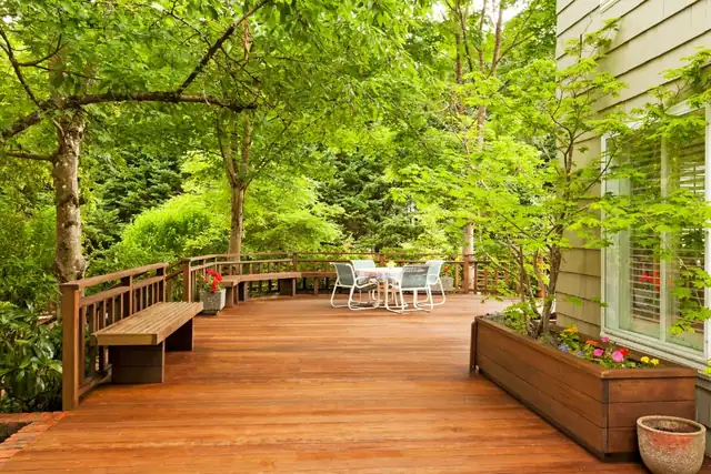 Stained wood deck with built-in planter box and bench under shade trees